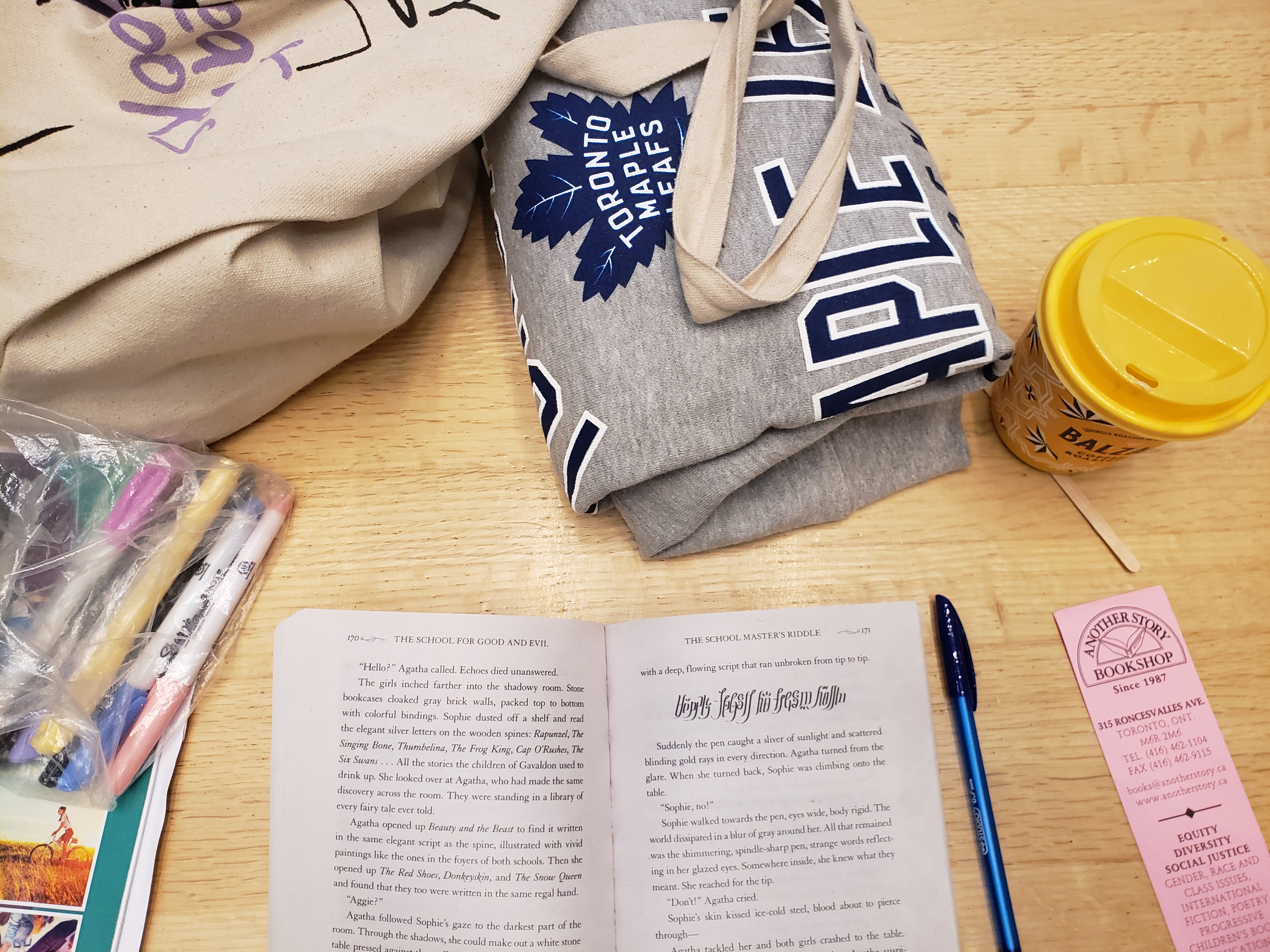 A book in a table with an eco bag, some pens, a hoodie and a balzacs coffee